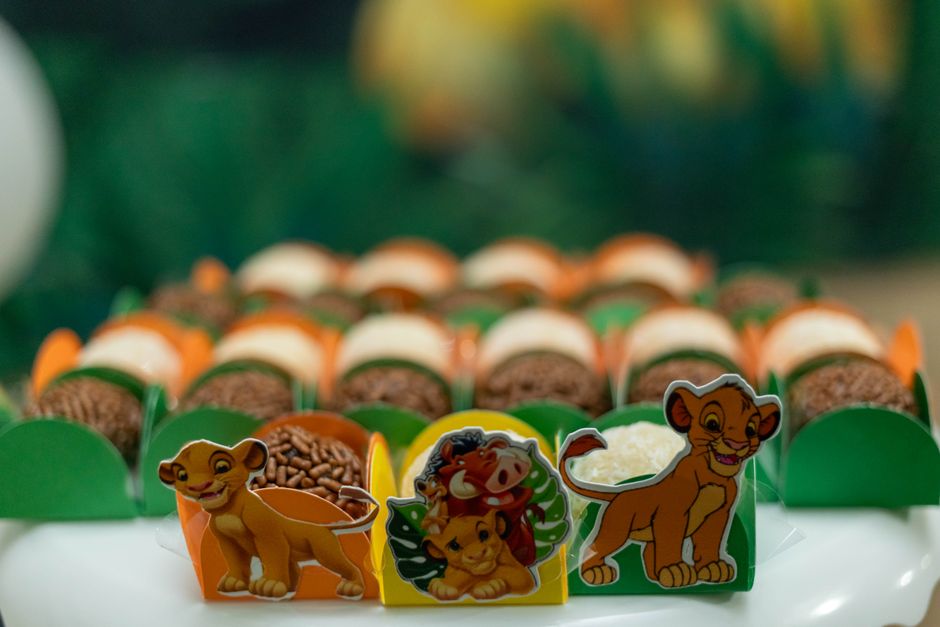 Imagem de uma mesa decorada com temas do filme O Rei Leão, com doces e figuras ilustrativas de personagens da animação, ideal para festa infantil com temática de animais e filmes de infância.