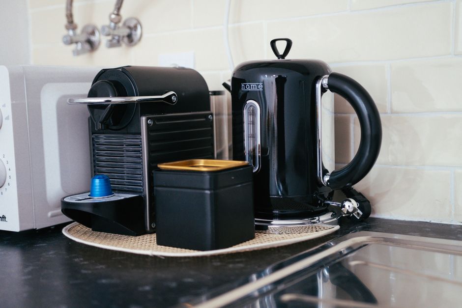 Imagem de uma cafeteira elétrica e uma máquina de café expresso em uma cozinha moderna, representando praticidade e rotina matinal.