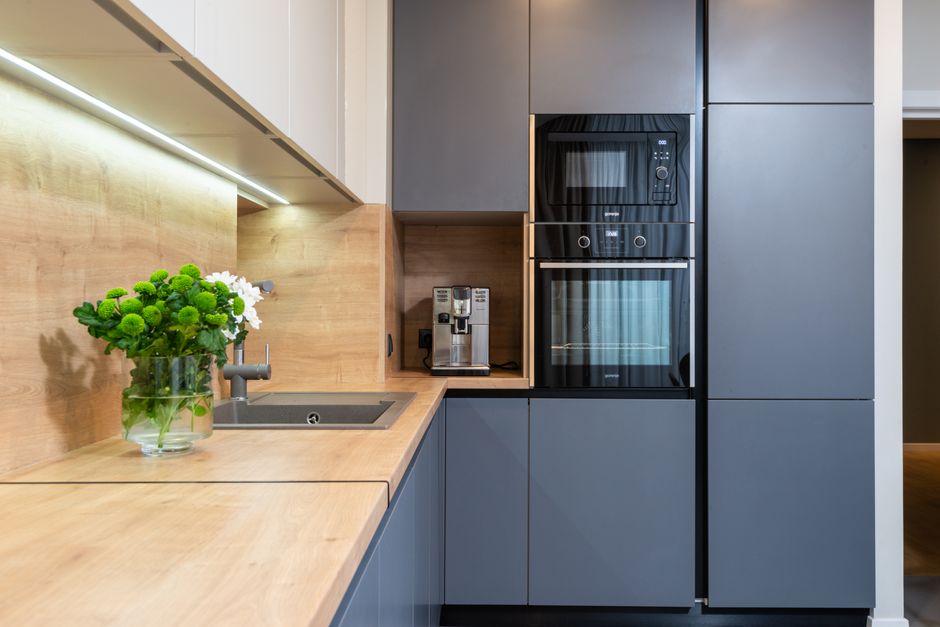 Imagem de uma cozinha moderna e minimalista com armários cinza, bancada de madeira clara, e eletrodomésticos embutidos, ideal para ilustrar design de interiores.