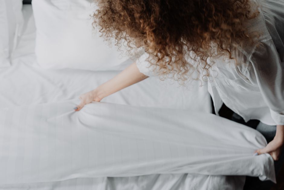 Mulher ajustando a roupa de cama, representando cuidado com o ambiente doméstico e bem-estar.