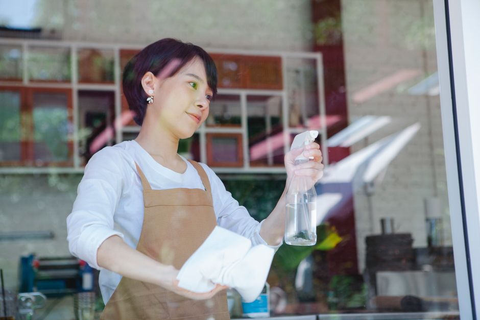 Mulher praticando a limpeza e higiene do ambiente de trabalho em um espaço que parece ser uma cozinha ou área de convivência moderna.