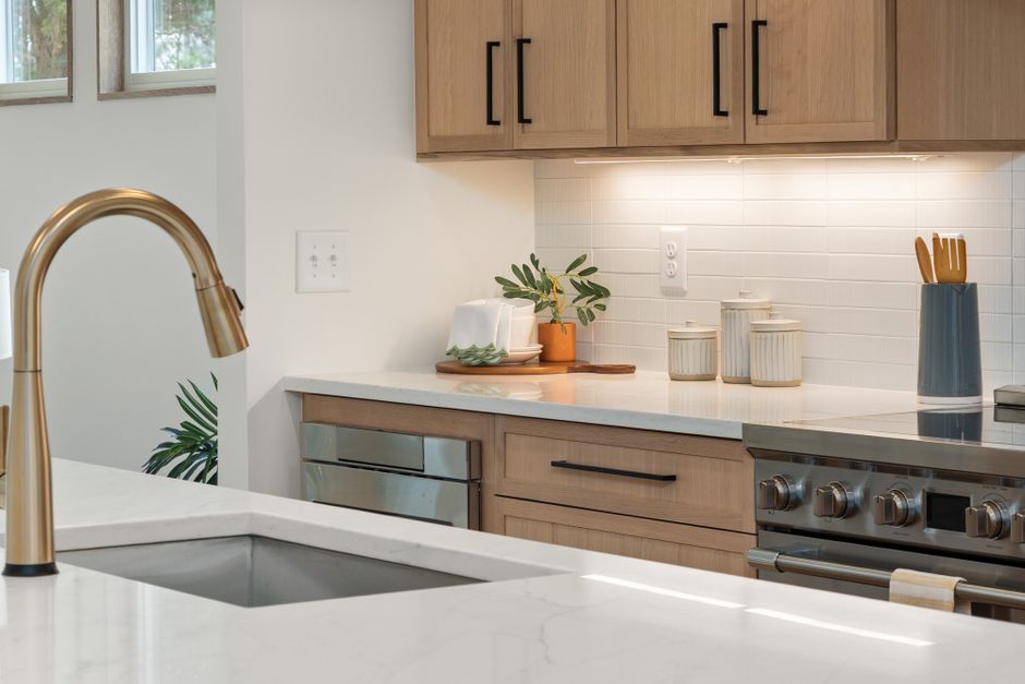 Imagem de uma cozinha moderna com armários de madeira, pia com torneira de acabamento dourado e detalhes minimalistas na decoração.