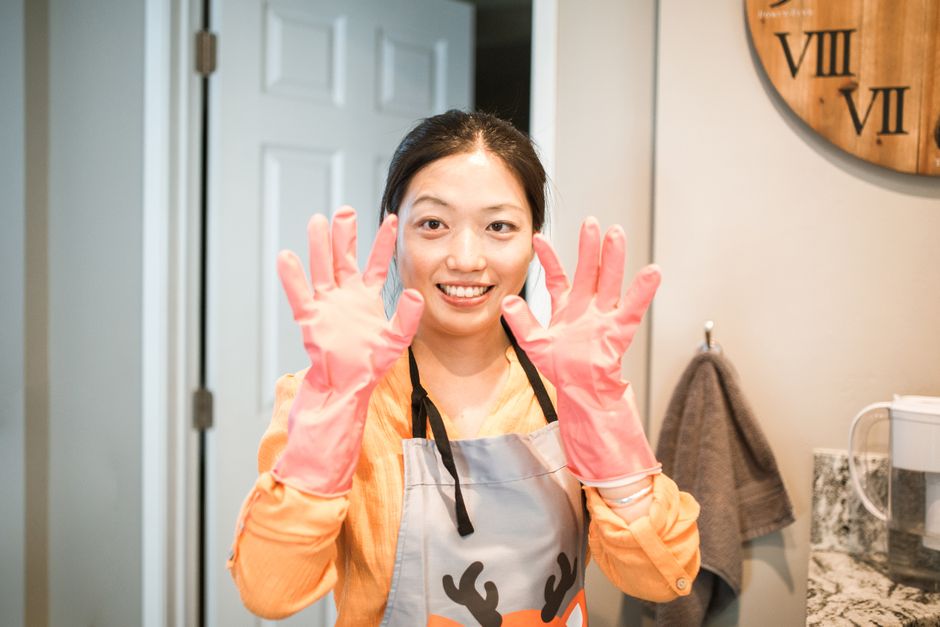 Mulher sorridente usando luvas de limpeza e avental, preparando-se para realizar tarefas domésticas ou de limpeza na cozinha de casa.
