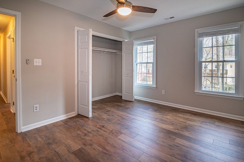 Quarto vazio com piso de madeira clara, duas janelas, closet embutido e iluminação natural, ideal para decoração e montagem de ambientes.