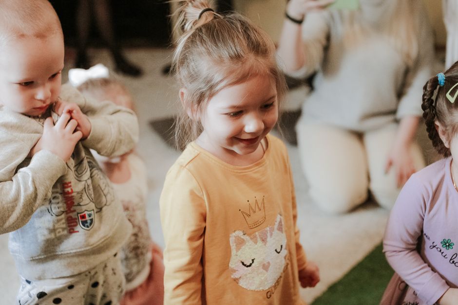Crianças participando de uma atividade lúdica em ambiente interno, com destaque para uma menina sorridente ao centro.