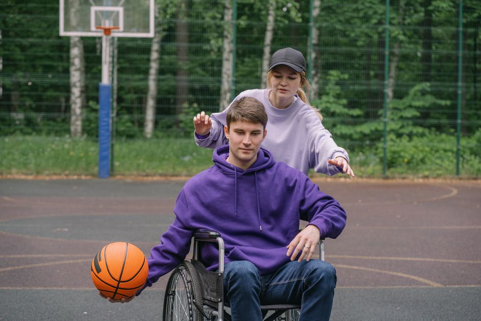 Jovem em cadeira de rodas brincando basquete ao ar livre, demonstrando inclusão e esporte para pessoas com deficiência.