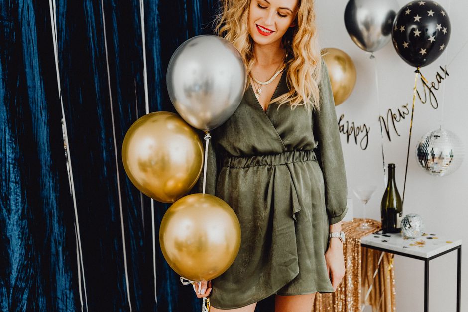 Mulher sorridente em uma celebração de Ano Novo, decorada com balões dourados e prateados.