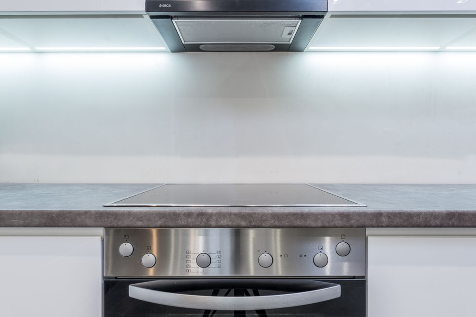 Imagem de uma cozinha moderna com fogão de vidro e sistema de exaustão embutido no teto, com iluminação de teto brilhante.