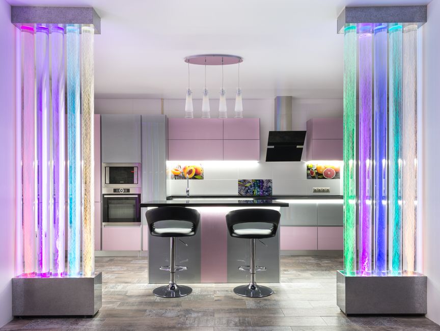 Imagem de uma cozinha moderna com iluminação colorida, centro de entretenimento e design futurista.