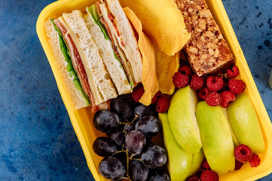 Imagem de uma marmita com sanduíches, frutas variadas e doces, ideal para abordar temas de alimentação saudável e refeições práticas para o dia a dia.