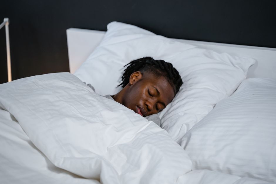 Pessoa dormindo tranquilamente em uma cama com roupas de cama brancas em um ambiente moderno.