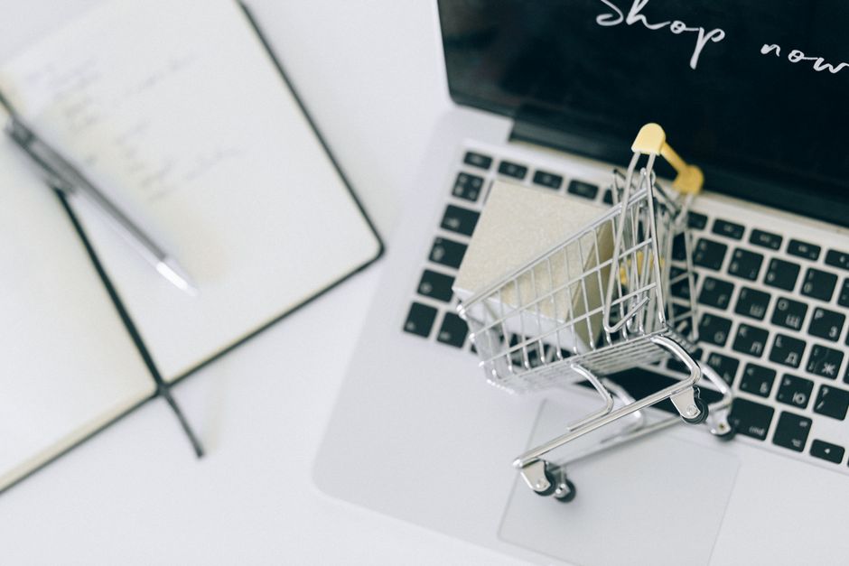 Imagem de um cenário de compras online com um carrinho de supermercado digital sobre um laptop, simbolizando e-commerce ou compras virtuais.