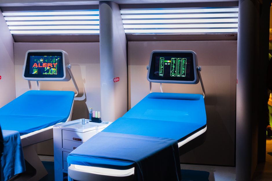 Imagem de uma sala de radioterapia moderna com duas cadeiras de tratamento e monitores digitais, ambientada em clínica de saúde avançada.