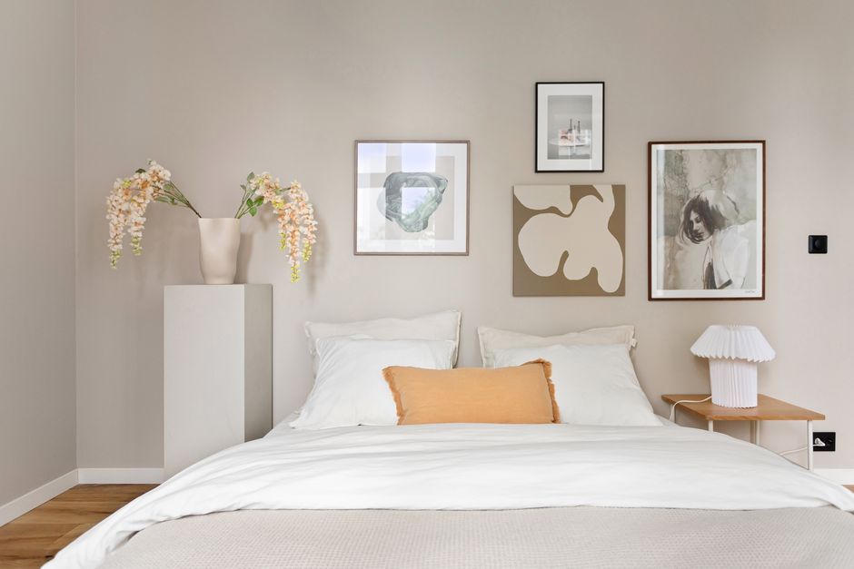Quarto confortável e bem decorado com quadros artísticos na parede, luminária de mesa e vaso com flores, ideal para mostrar dicas de decoração de interiores ou organização de ambientes.
