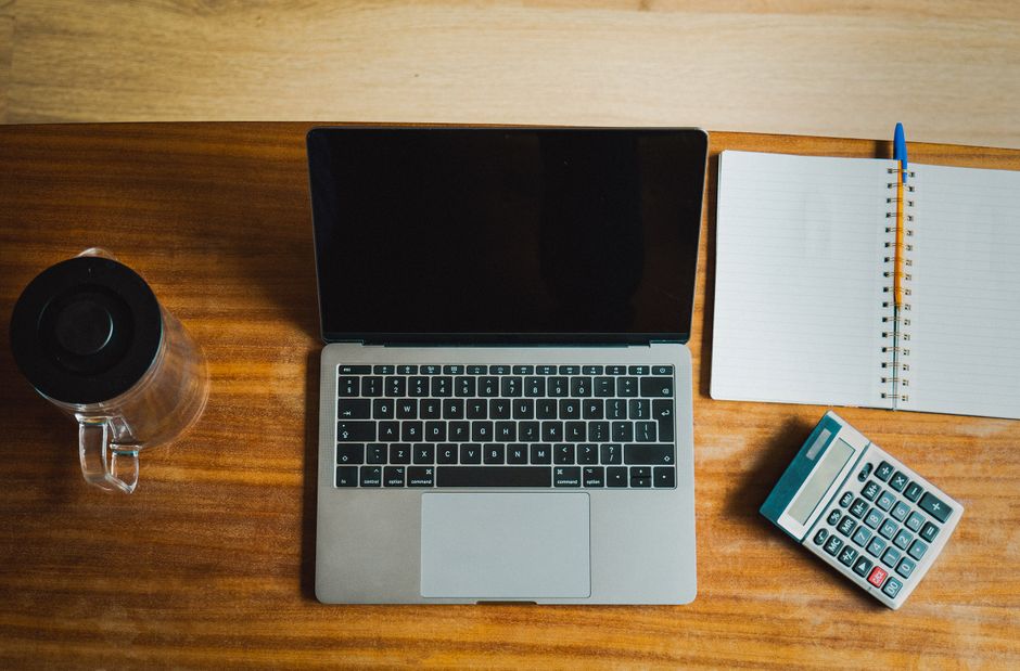 Imagem de um espaço de trabalho com computador, caderno, caneta, calculadora e uma garrafa térmica, ideal para artigos sobre organização e produtividade no escritório.