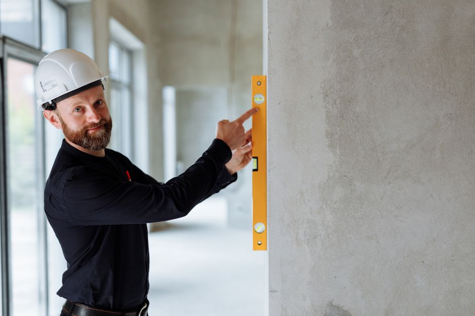 Profissional de construção civil usando nível a laser para verificar a nivelação de uma parede em uma obra em andamento.