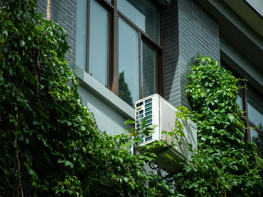 Imagem de uma fachada de prédio residencial com jardim vertical e ar-condicionado externo em destaque, sugerindo sustentabilidade e conforto urbano.
