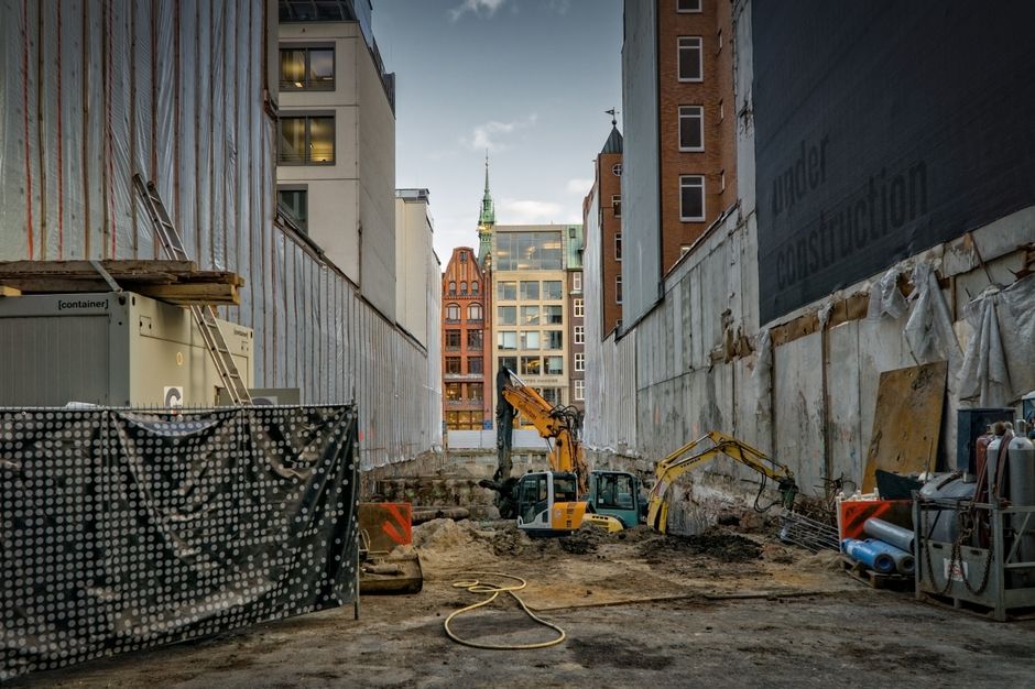 Imagem de uma obra de construção em área urbana, com escavadeiras em atividade entre prédios modernos, simbolizando desenvolvimento urbano e infraestrutura.