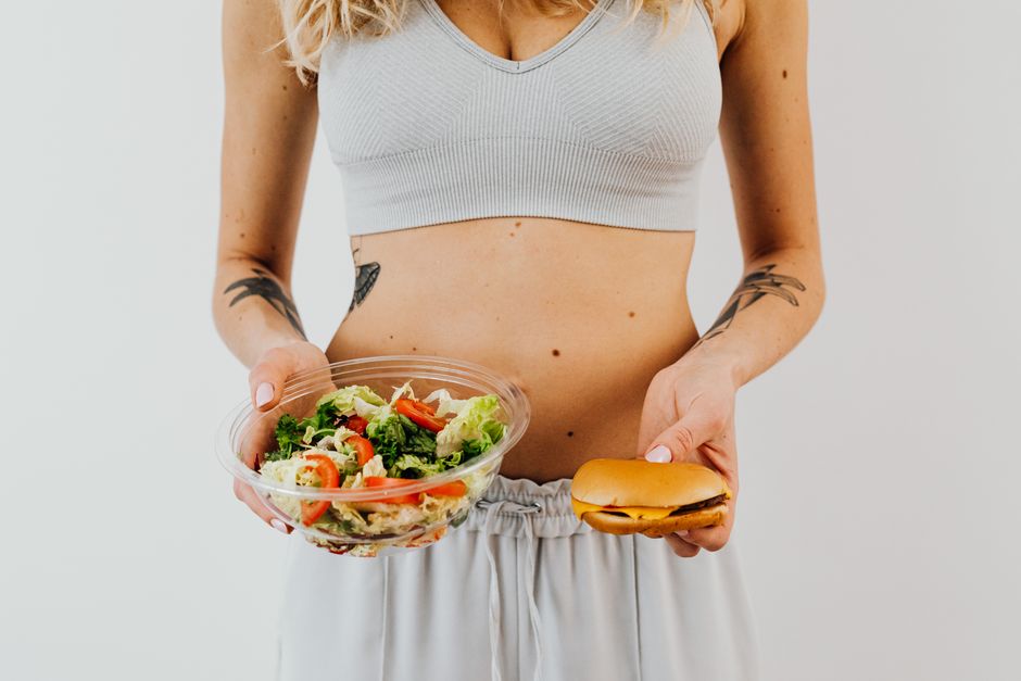 Mulher segurando uma tigela de salada e um sanduíche, representando escolhas alimentares equilibradas e estilo de vida saudável.