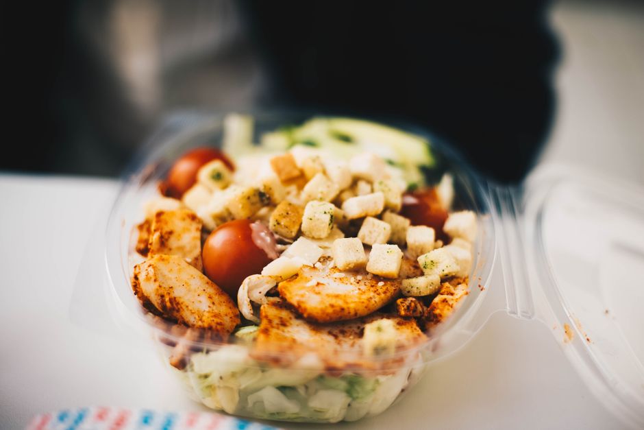 Foto de uma salada colorida em recipiente plástico, composta por ingredientes frescos e molho, ideal para conteúdo sobre alimentação saudável ou preparação de refeições.