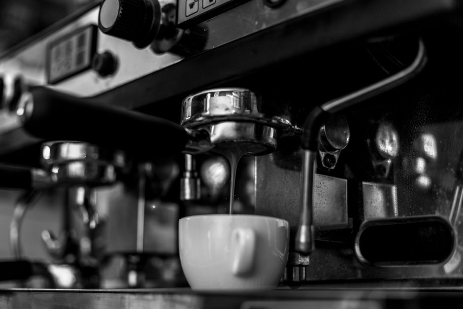 Imagem de uma máquina de café expresso preparando um café em uma cozinha ou cafeteria.