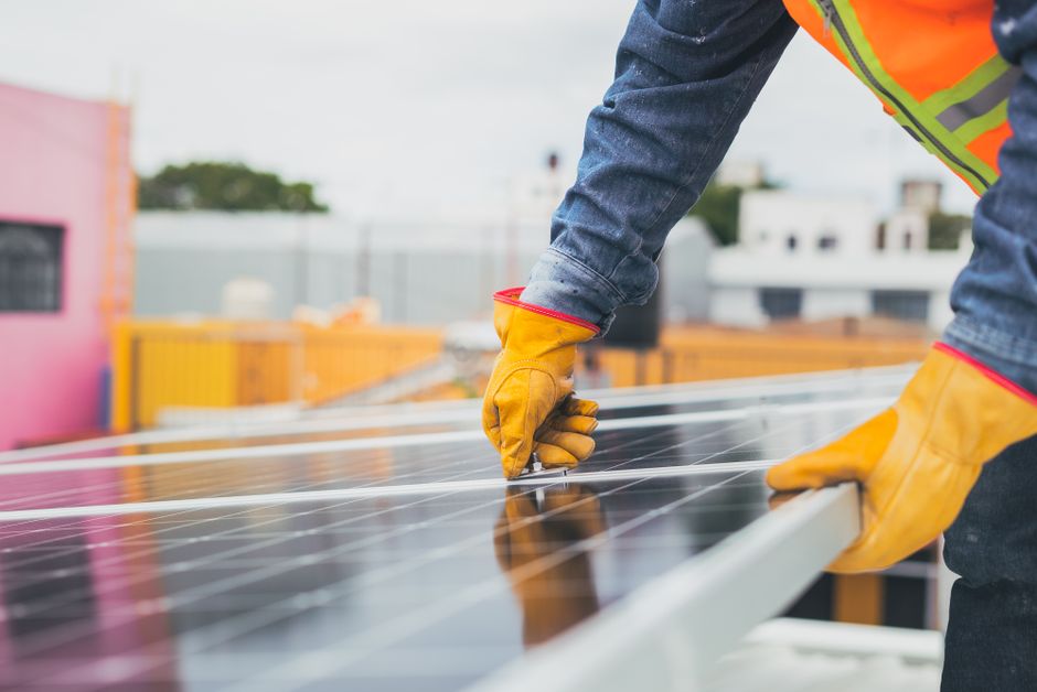 Imagem de um trabalhador instalando painéis solares em um telhado, destacando a energia renovável e sustentabilidade.
