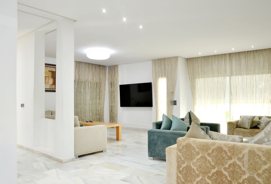 Sala de estar moderna e aconchegante com grandes janelas, sofás confortáveis e televisão de tela plana, ideal para artigos sobre decoração e bem-estar em ambientes domésticos.