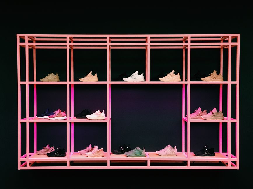 Estante moderna exibindo diferentes cores de tênis esportivos sobre fundo escuro com iluminação neon rosa.
