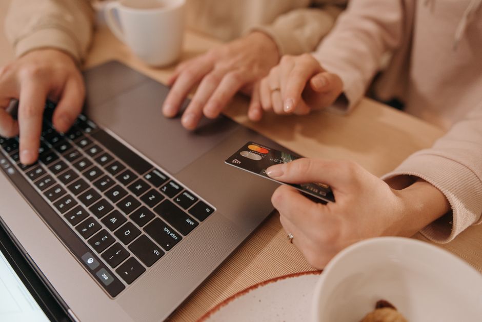 Duas pessoas realizando uma compra online com cartão de crédito em um ambiente de convívio, simbolizando comércio eletrônico e segurança nas transações digitais.