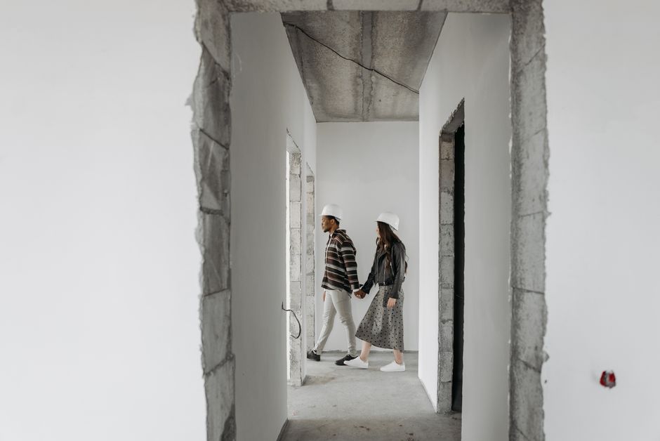 Casal de arquitetos ou engenheiros avaliando o andamento de uma construção residencial em um prédio ainda em obras, em um ambiente com paredes brancas e estrutura de concreto exposta.