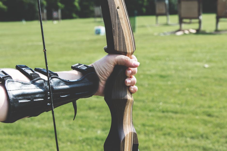 Pessoa segurando um arco e flecha ao ar livre, preparado para atirar, durante uma atividade de tiro com arco.