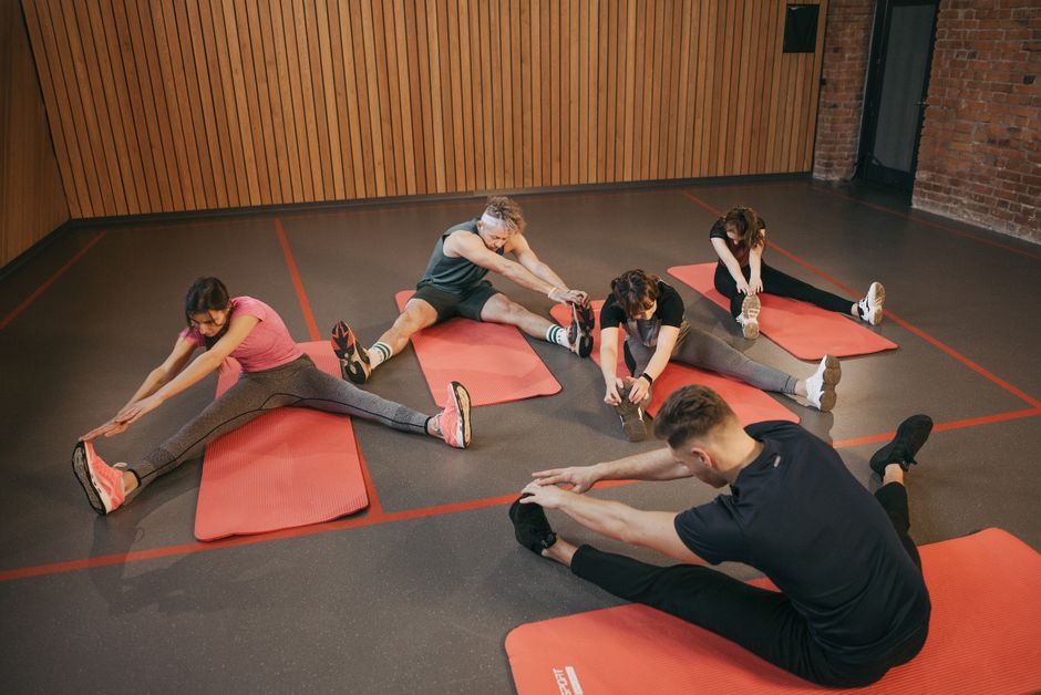 Grupo de pessoas realizando alongamento ou exercício de yoga em ambiente indoor para promover bem-estar e saúde.
