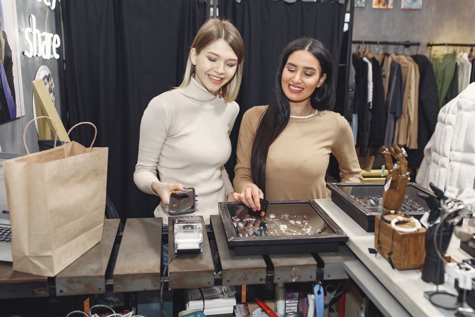 Duas mulheres sorridentes comprando joias em uma loja de moda e acessórios, demonstrando satisfação durante a aquisição.