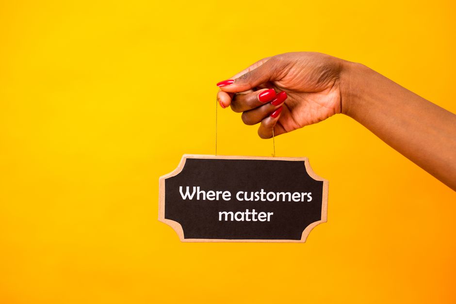 Mão segurando um painel com a frase 'Where customers matter' em fundo amarelo, destacando a importância do cliente no contexto empresarial.