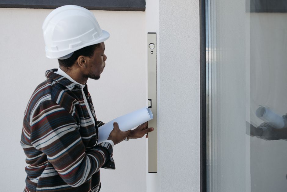 Profissional de engenharia ou arquitetura avaliando uma entrada de edifício com um nível de bolha, simbolizando inspeção ou controle de qualidade em construção civil.