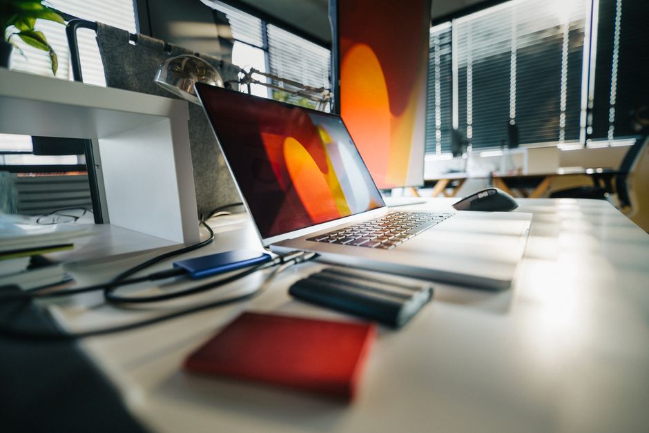Imagem de um escritório moderno com um laptop, monitor, mouse e itens de escritório, ideal para artigos sobre ambiente de trabalho e produtividade.