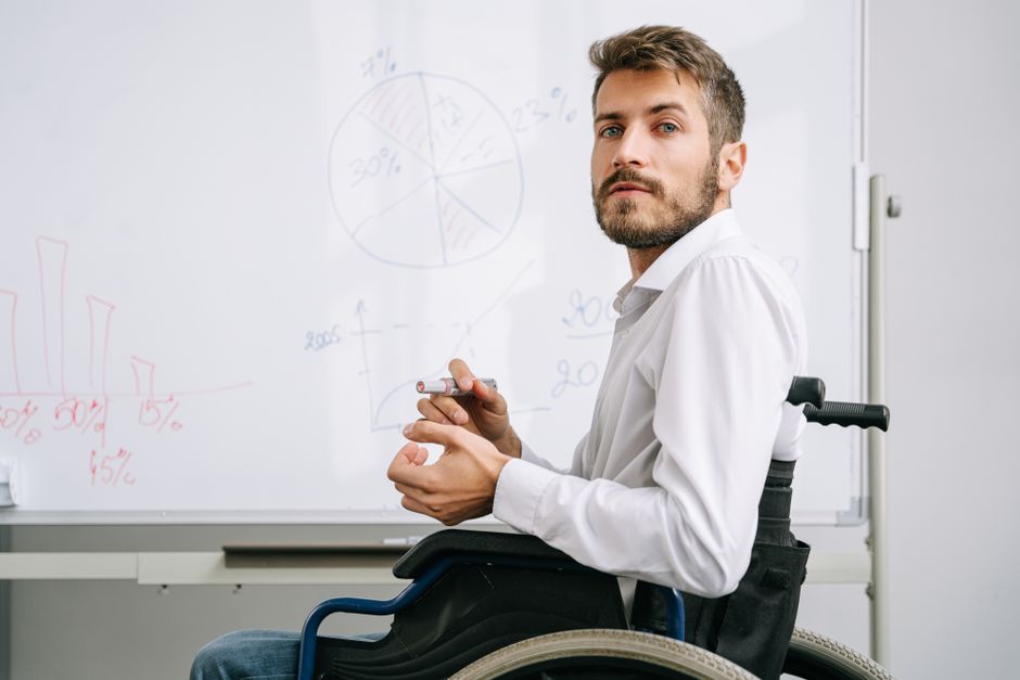 Homem em cadeira de rodas realizando uma apresentação de gráficos e dados em um quadro branco, simbolizando acessibilidade e inclusão no ambiente de negócios ou educação.