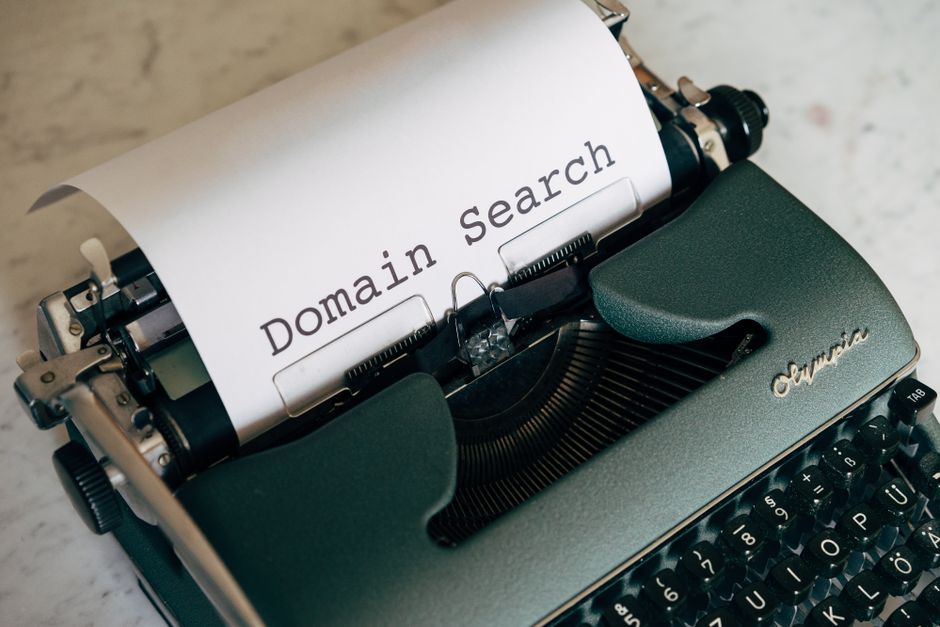 Máquina de escrever antiga com papel mostrando a frase 'Domain Search', simbolizando busca por domínios na internet.