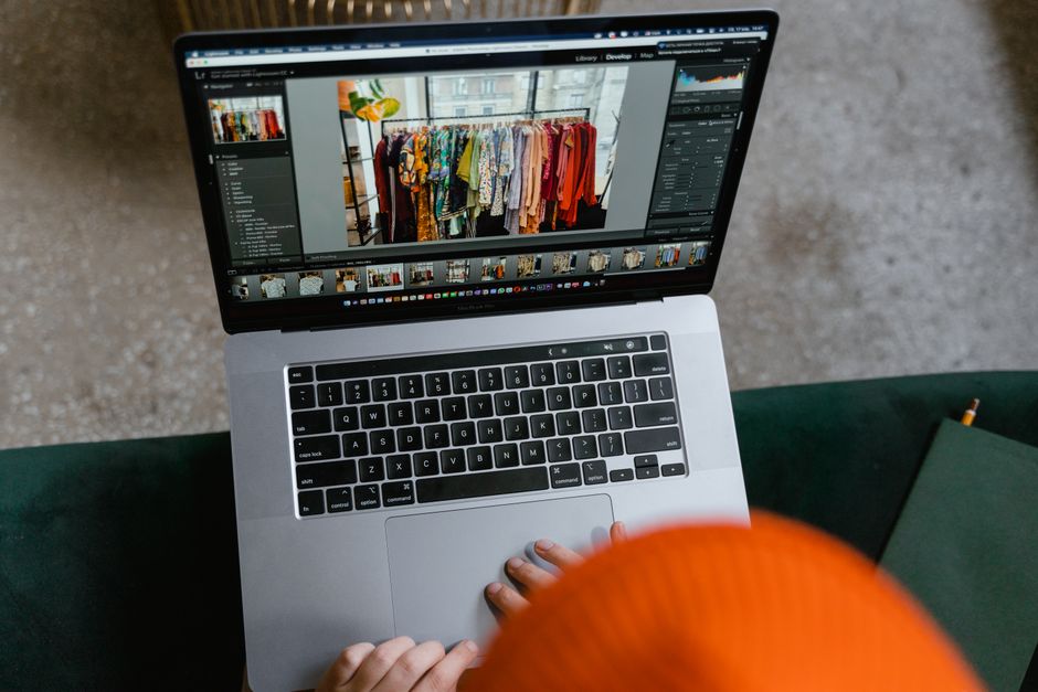 Pessoa editando fotos de roupas em um computador portátil, representando produção de conteúdo para moda ou e-commerce.