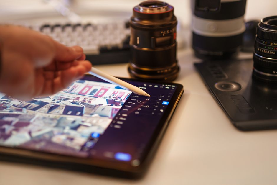 Pessoa editando fotos ou vídeos com um software de edição digital em um tablet, com equipamentos de fotografia ao redor.