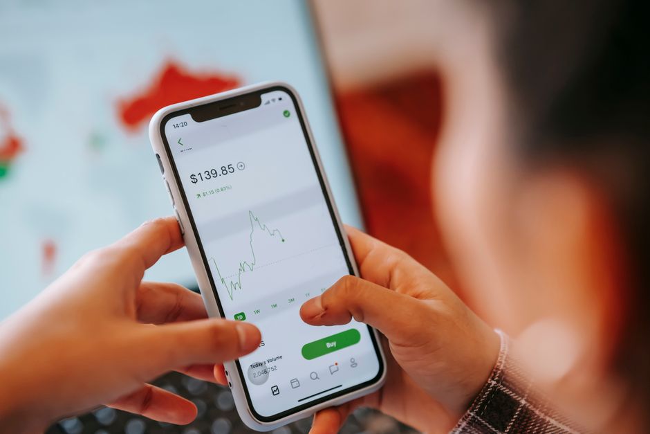 Pessoa monitorando investimentos financeiros pelo smartphone, simbolizando gestão de finanças pessoais ou investimentos online.