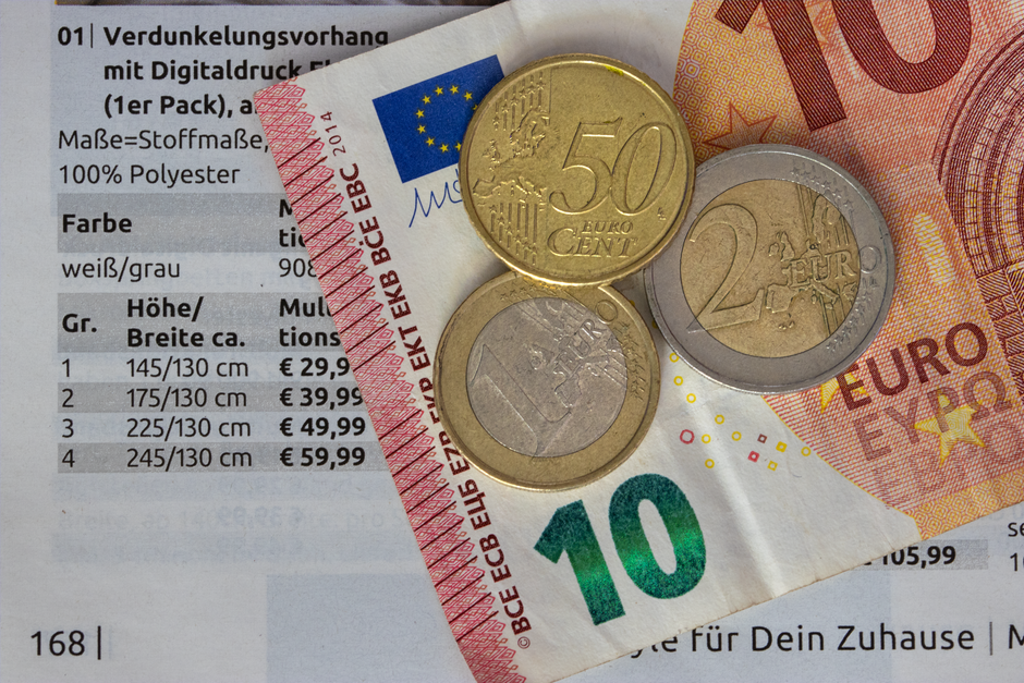 Imagem representando temas financeiros e de gestão, com destaque para moedas e cédulas de euro sobre uma página de catálogo de produtos.