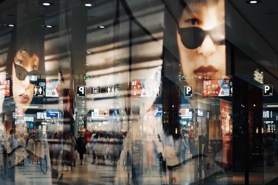 Imagem de um aeroporto com reflexo de anúncios e um rosto de mulher usando óculos escuros, criando uma atmosfera de movimento e modernidade.