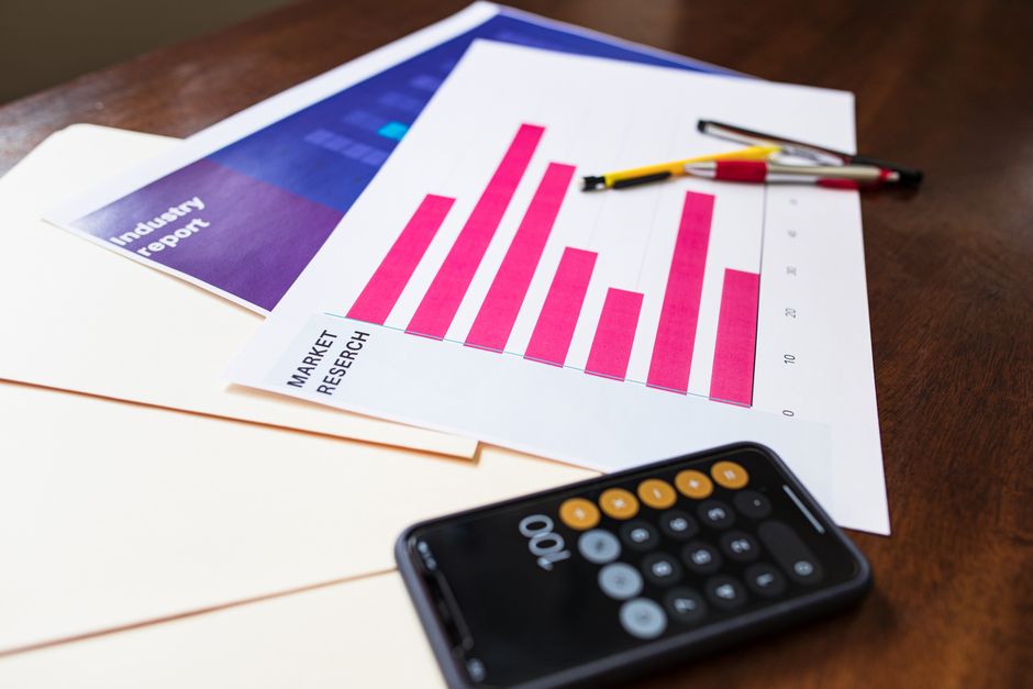 Imagem de uma mesa de trabalho com gráficos, calculadora e celular, sugerindo análise de dados e planejamento financeiro.