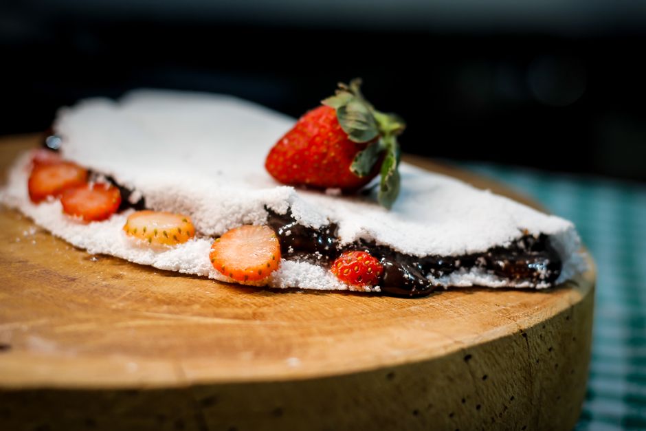 Imagem de uma torta de morango com calda de chocolate e cobertura de açúcar de confeiteiro, decorada com uma morango sobre uma tábua de madeira, representando sobremesas e culinária artesanal.