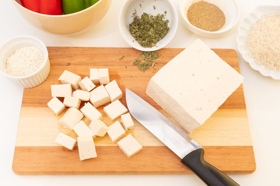 Imagem de queijo em cubos sobre uma tábua de corte, acompanhada de temperos e ingredientes para culinária, com foco na preparação de pratos tradicionais.