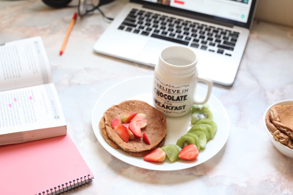 Cena de uma mesa de trabalho com café da manhã saudável, incluindo frutas, biscoitos e um laptop aberto, ideal para um artigo sobre produtividade e bem-estar no trabalho.