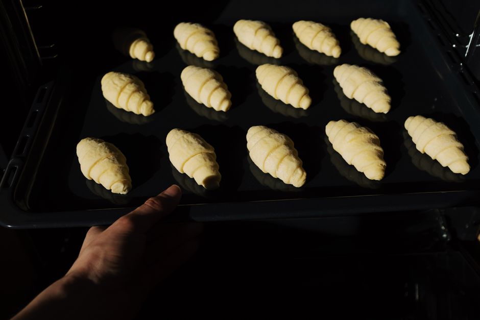 Pessoas preparando croissants no forno, ilustrando o processo de confeitaria caseira ou gastronomia.
