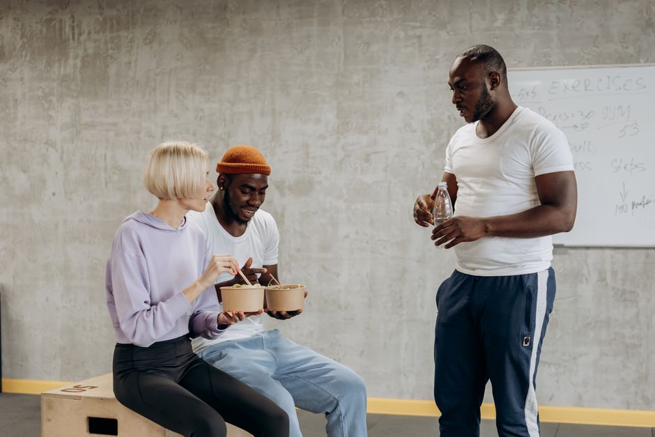Três jovens participando de uma conversa descontraída em um ambiente de coworking ou espaço de treinamento, promovendo interação e socialização.