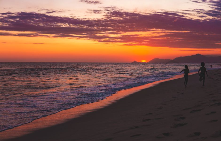 Pôr do sol na praia com duas crianças brincando na areia, capturando momentos de lazer e contato com a natureza.